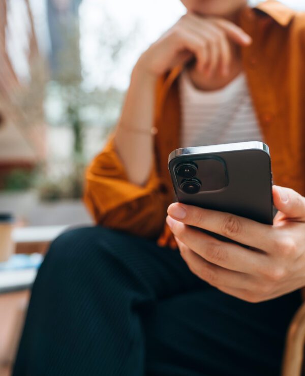Close up shot of a young woman using smartphone while sitting in an outdoor cafe and drinking coffee.